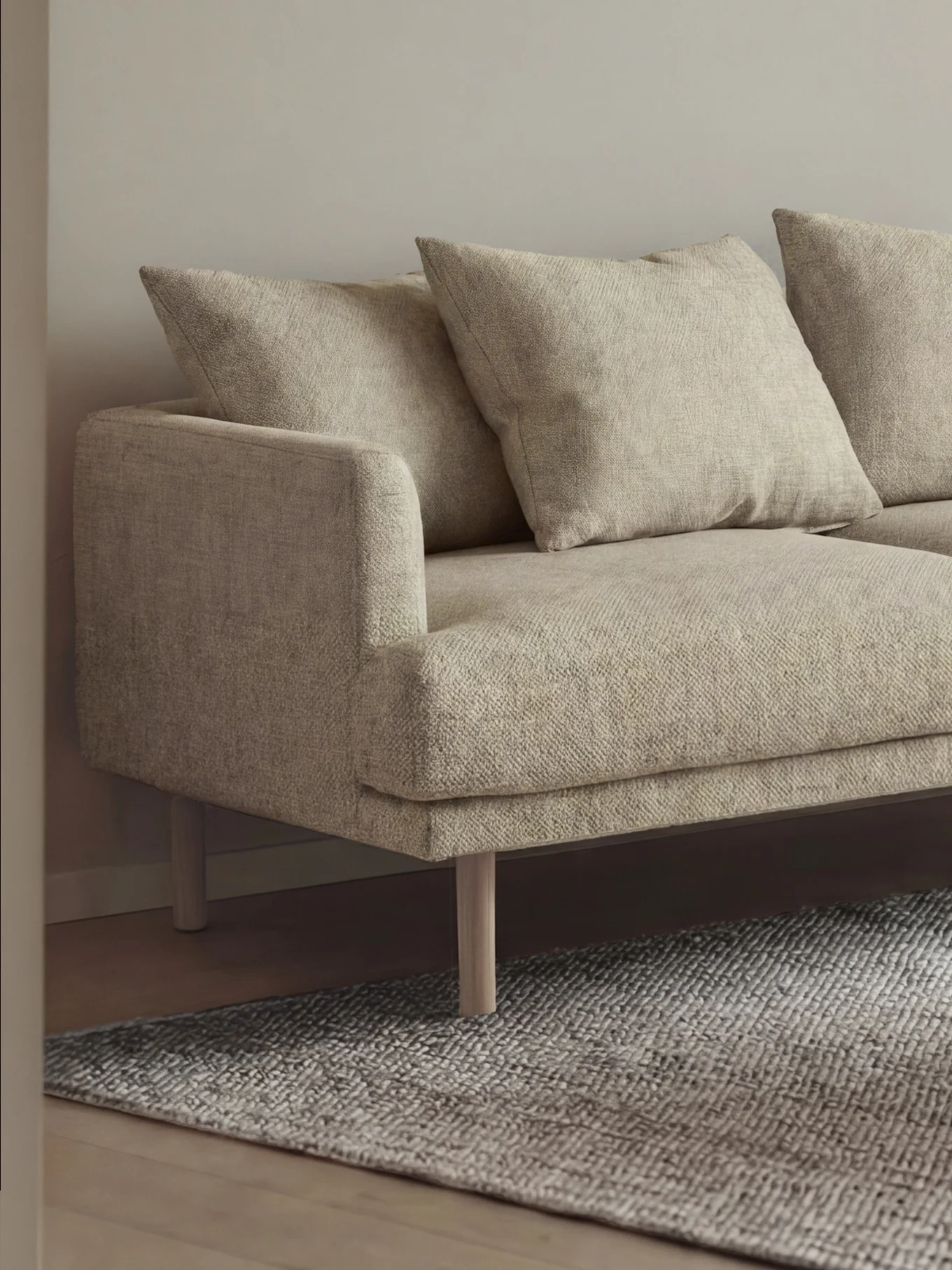 Minimalistisk stue med lys beige sofa, rundt sofabord i tre med bok, hvit gulvlampe og lyse gardiner.